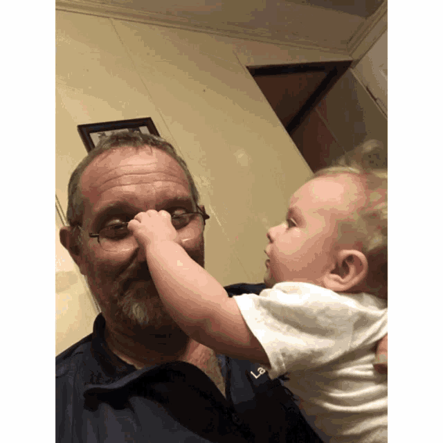 a man with glasses is holding a baby and the baby is touching the man 's nose
