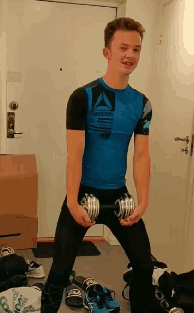 a young man in a blue reebok shirt holds a dumbbell in his hands