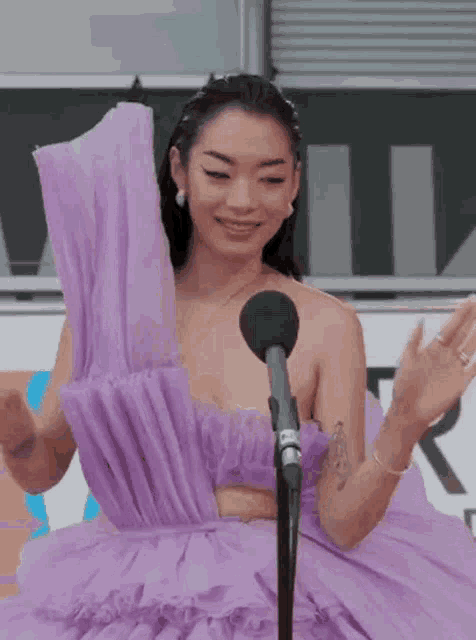 a woman in a purple dress is standing in front of a microphone waving her hands .