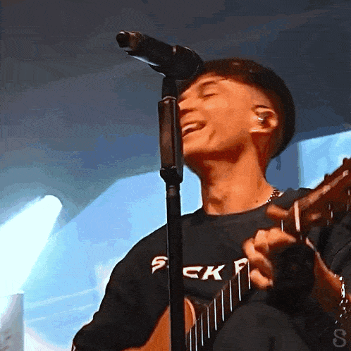 a man singing into a microphone wearing a black shirt that says suck