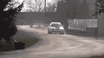 a car is driving down a dirt road with trees in the background .