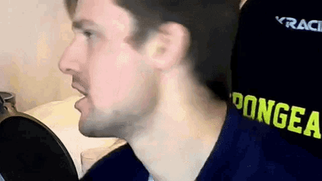 a man is sitting in front of a microphone wearing a black shirt with the word dongea on the back .