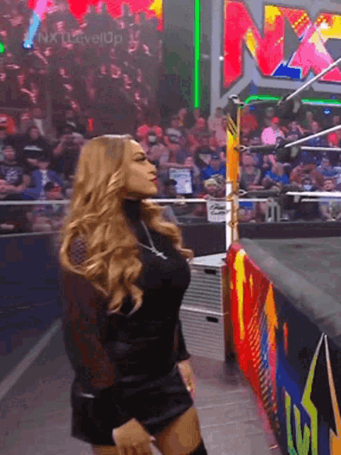 a woman in a black dress is dancing in front of a crowd with a sign that says nxt on it