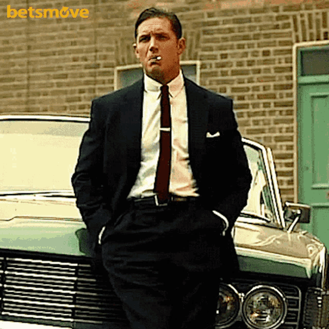 a man in a suit and tie is smoking a cigarette in front of a car with the word betsmove in the background