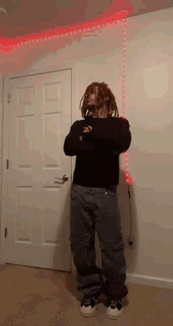 a man with dreadlocks is standing in front of a white door with his arms crossed