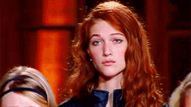 a woman with long red hair is standing in front of a group of women