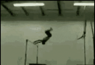 a gymnast is doing a trick on a parallel bars in a gym .