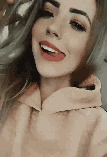 a woman in a pink hoodie is smiling and sticking her tongue out
