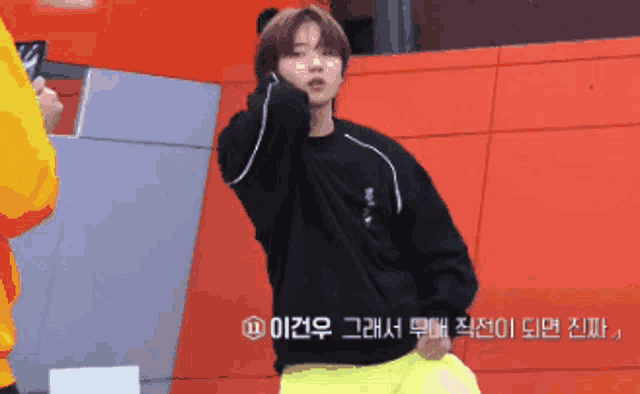 a man wearing a black sweater and yellow pants is standing in front of a red wall