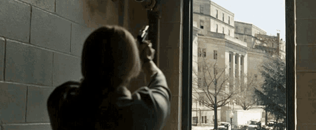 a woman is looking out a window at a large building
