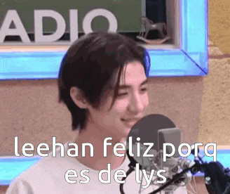 a young man is standing in front of a microphone with the words leehan feliz porq es de lys written on it .