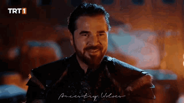 a man with a beard is smiling in front of a fire with a trt1 logo in the background .