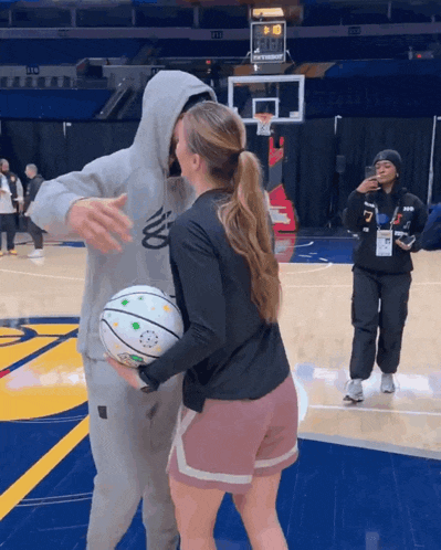 a man and woman are hugging on a basketball court with a scoreboard behind them that says ' nba ' on it