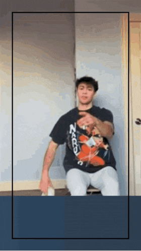 a man wearing a naruto t-shirt is sitting on a chair in a room .
