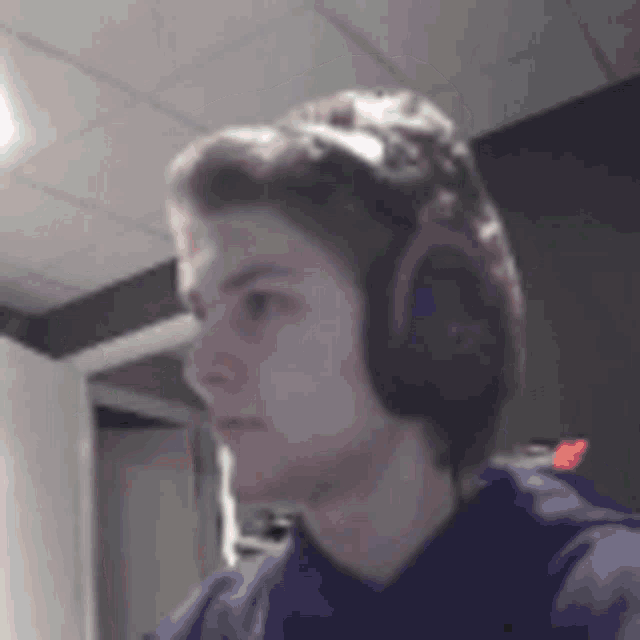 a young man wearing headphones and a purple shirt is looking at the camera .