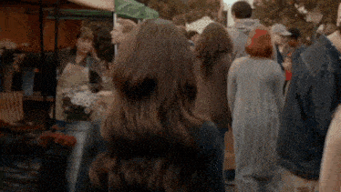 a woman with long brown hair is standing in a crowd of people at a market .