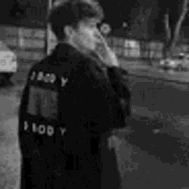 a black and white photo of a man smoking a cigarette while wearing a black jacket .