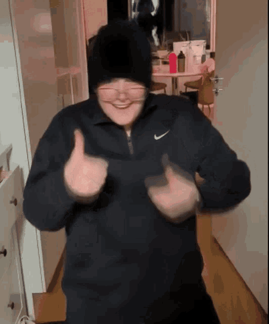 a person wearing a black nike sweatshirt is giving a thumbs up sign