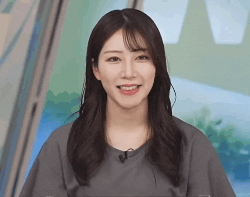 a woman wearing a grey shirt with a microphone on her neck smiles