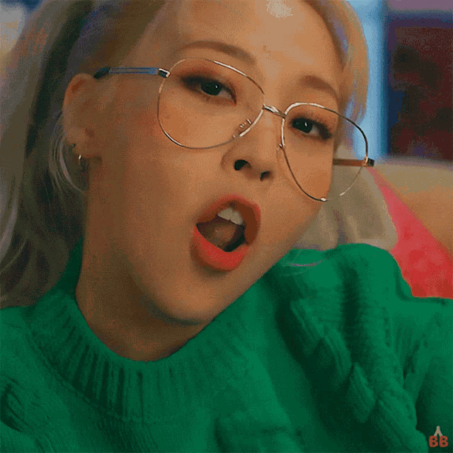 a close up of a woman wearing glasses and a green sweater with the letters bb on it