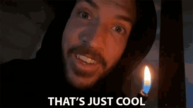 a man in a hooded jacket is standing in front of a lit candle and saying that 's just cool .