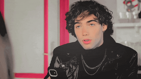 a young man with curly hair is wearing a black jacket and a turtleneck