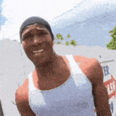 a man wearing a hat and a white tank top smiles