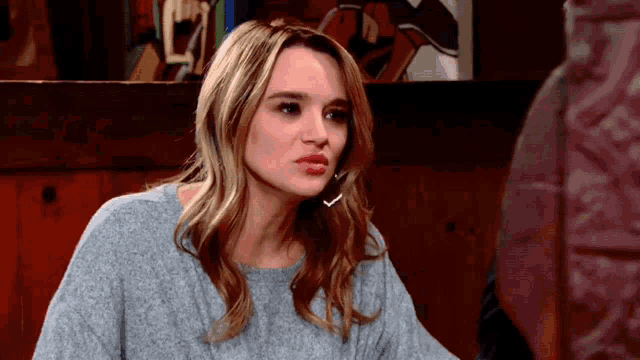 a woman in a grey sweater is sitting in front of a wall