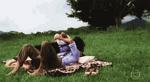 a man and woman are laying on a blanket in a field with the letter o in the corner