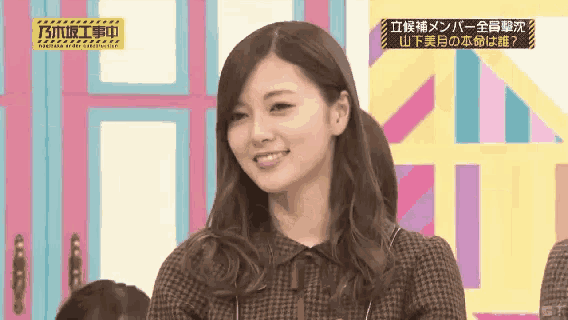 a woman in a plaid shirt is smiling in front of a yellow sign that says ' n ' on it .