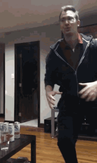 a man in a black jacket is dancing in a living room with budweiser cans on a table