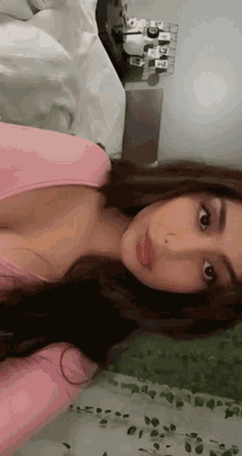 a woman in a pink shirt is taking a selfie while sitting on a bed .