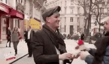 a man in a suit and hat is holding another man 's hand on a street .