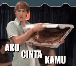 a man is holding a pizza box with the words aku cinta kamu written on it .