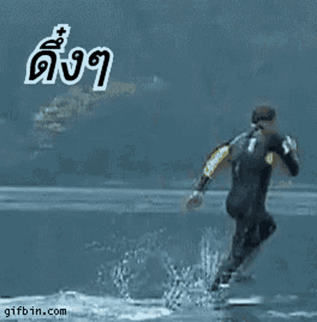 a man in a wetsuit is running in the water with a gifbin.com logo in the corner