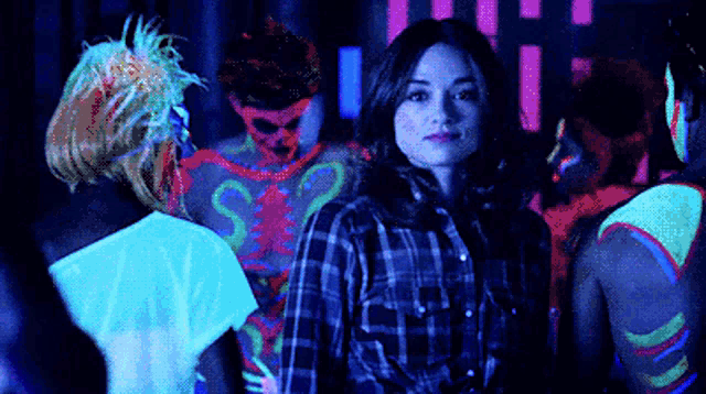 a woman in a plaid shirt is standing in a dark room with glow in the dark paint on her body