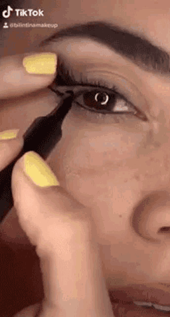 a woman with yellow nails is applying eyeliner on her eye