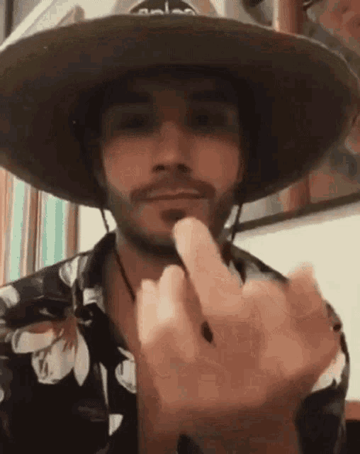 a man with a beard wearing a cowboy hat is giving the middle finger