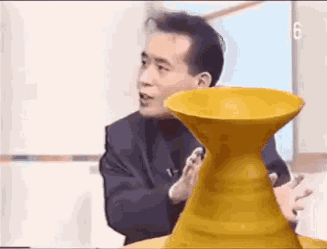 a man in a suit is standing next to a yellow vase .