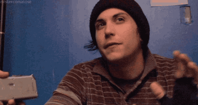 a man wearing a beanie and gloves is holding a cell phone .