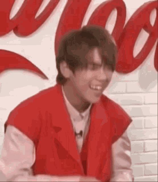 a young man wearing a red vest and a white shirt is laughing .