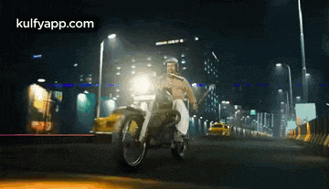 a man riding a motorcycle down a city street at night .