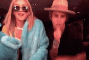 a woman wearing sunglasses and a hat is standing next to another woman wearing sunglasses and a hat .