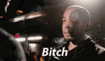 a bald man is smoking a cigarette in a dark room and says `` bitch '' .