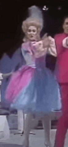 a woman in a pink and blue dress is dancing on a stage with a man in a red suit .