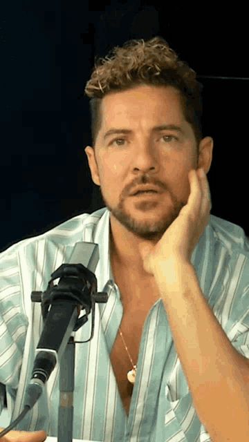 a man with a beard is sitting in front of a microphone with his hand on his chin