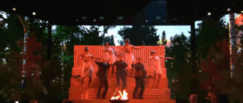 a group of people are dancing on a stage with trees in the background