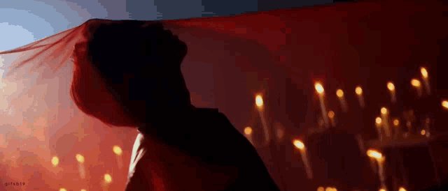a woman is standing in front of a row of candles with a red cloth covering her face .
