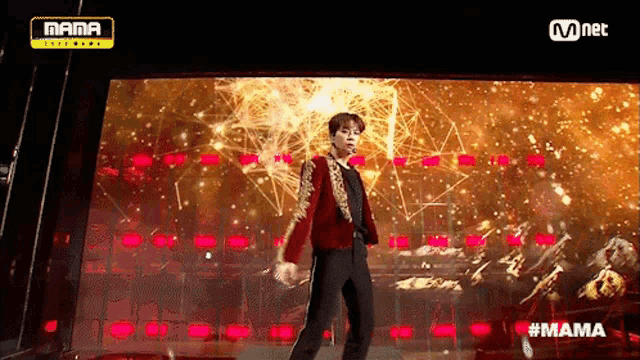 a man in a red jacket is dancing on a stage in front of a large screen that says mama