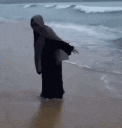 a woman in a hijab is standing on the beach .